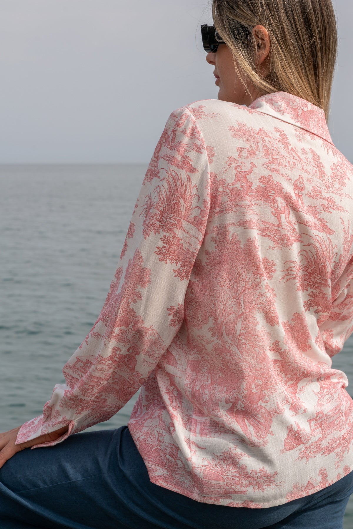 Camicia Elisabeth in Toile de Jouy rosa indossata da una donna al mare, elegante e romantica.