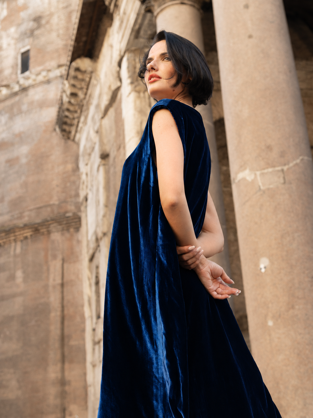Modella che indossa un abito lungo velluto seta elegante in blu, sullo sfondo di un edificio storico.