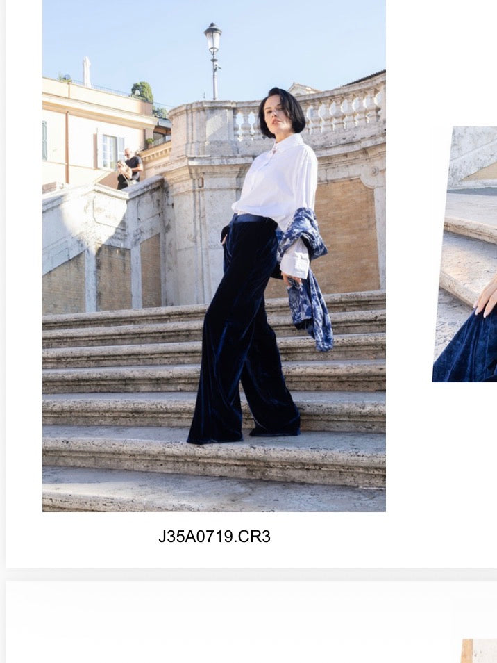 Modella su scale in pantalone velluto blu palazzo elegante con blusa bianca e giacca blu.