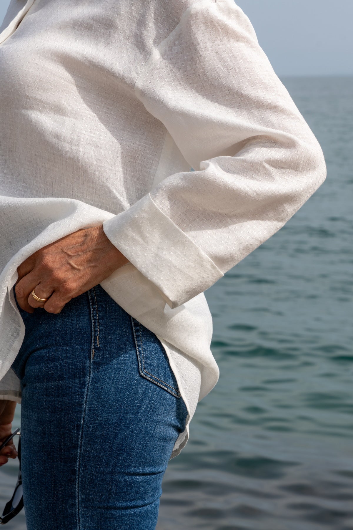 Camicia Capri in lino ricamata bianca indossata al mare, elegante e leggera, perfetta per l'estate.