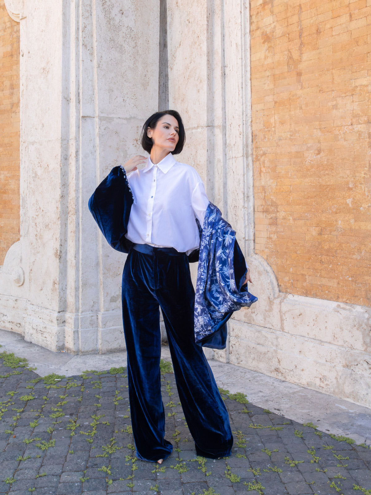 Pantalone velluto marrone palazzo indossato con camicia bianca e vicolo elegante, stile raffinato.