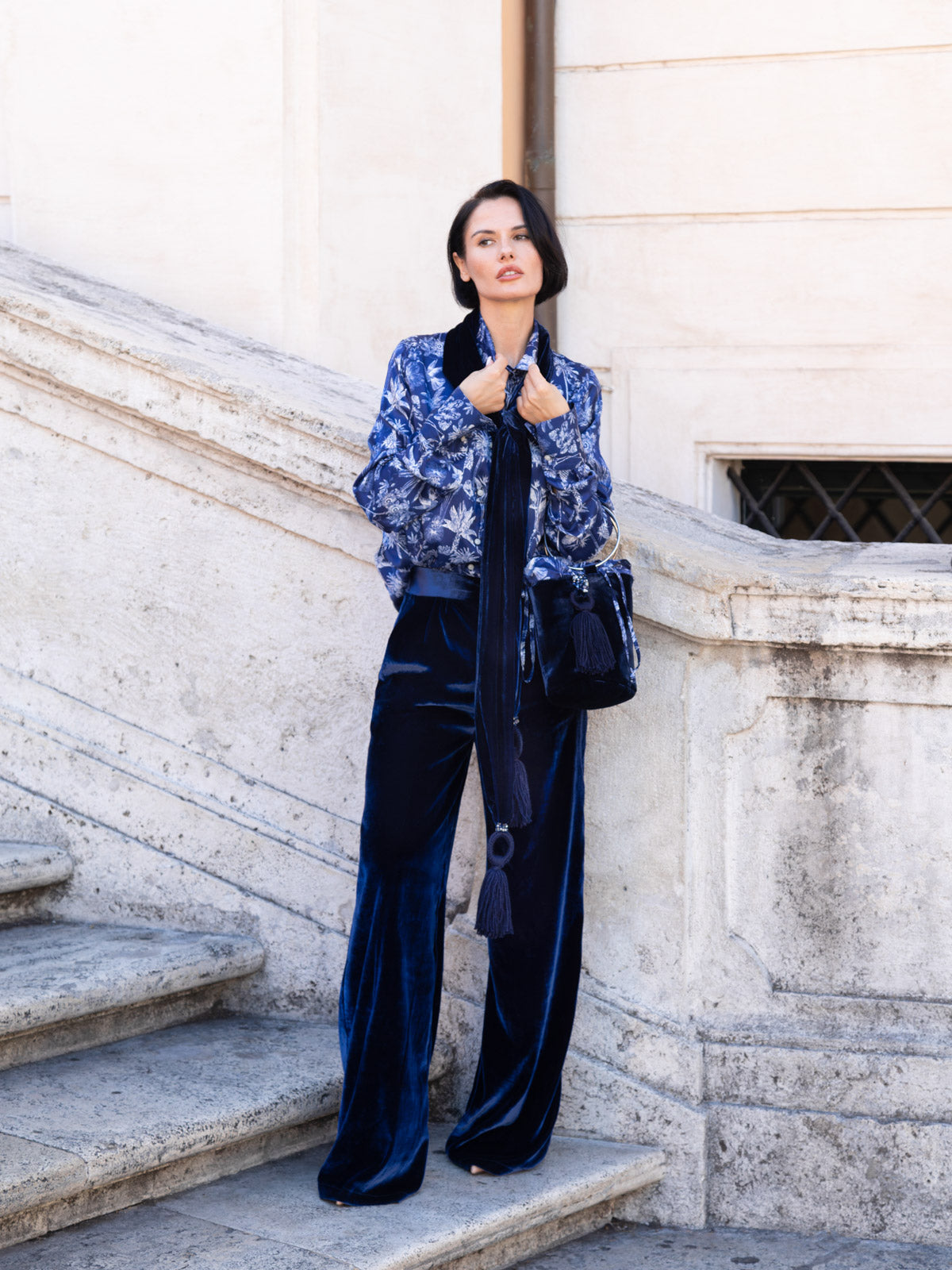 Donna in sciarpa in velluto di seta blu con nappine gioiello, posizionata su scale di marmo.