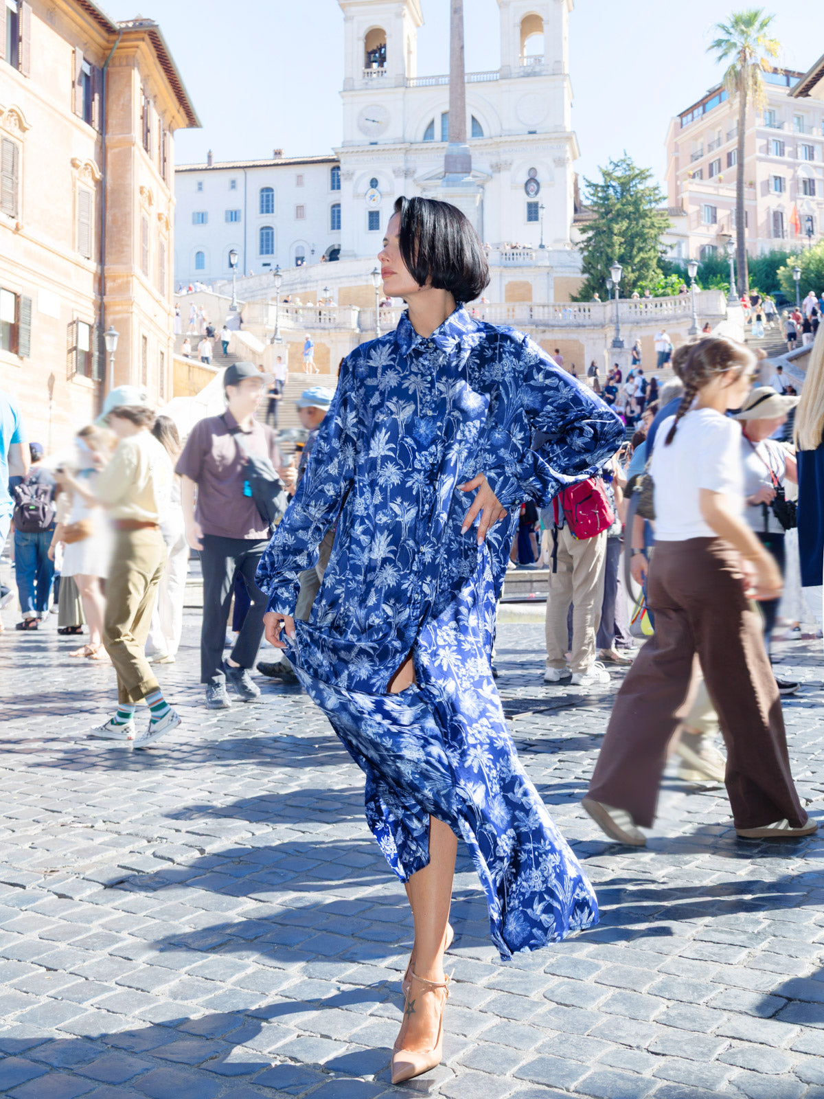 Donna che indossa chemisier lungo viscosa Liberty con stampa blu, elegante in un contesto urbano affollato.