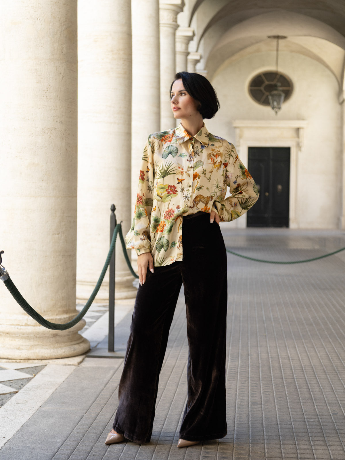 Modella con camicia floreale e pantalone velluto marrone palazzo in un ambiente elegante.