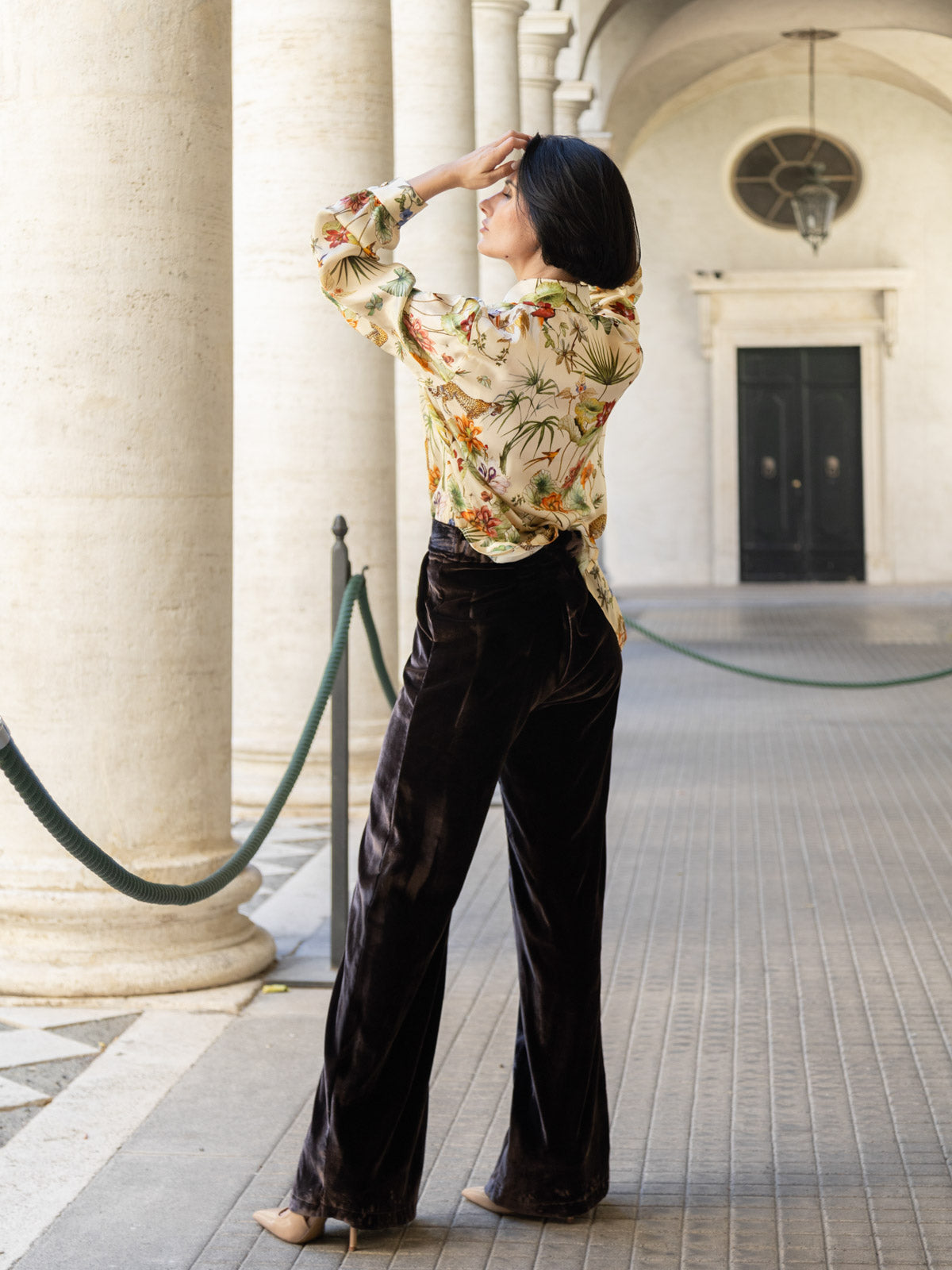 Pantalone velluto marrone palazzo indossato da donna, elegante e fluido, abbinato a camicia floreale.