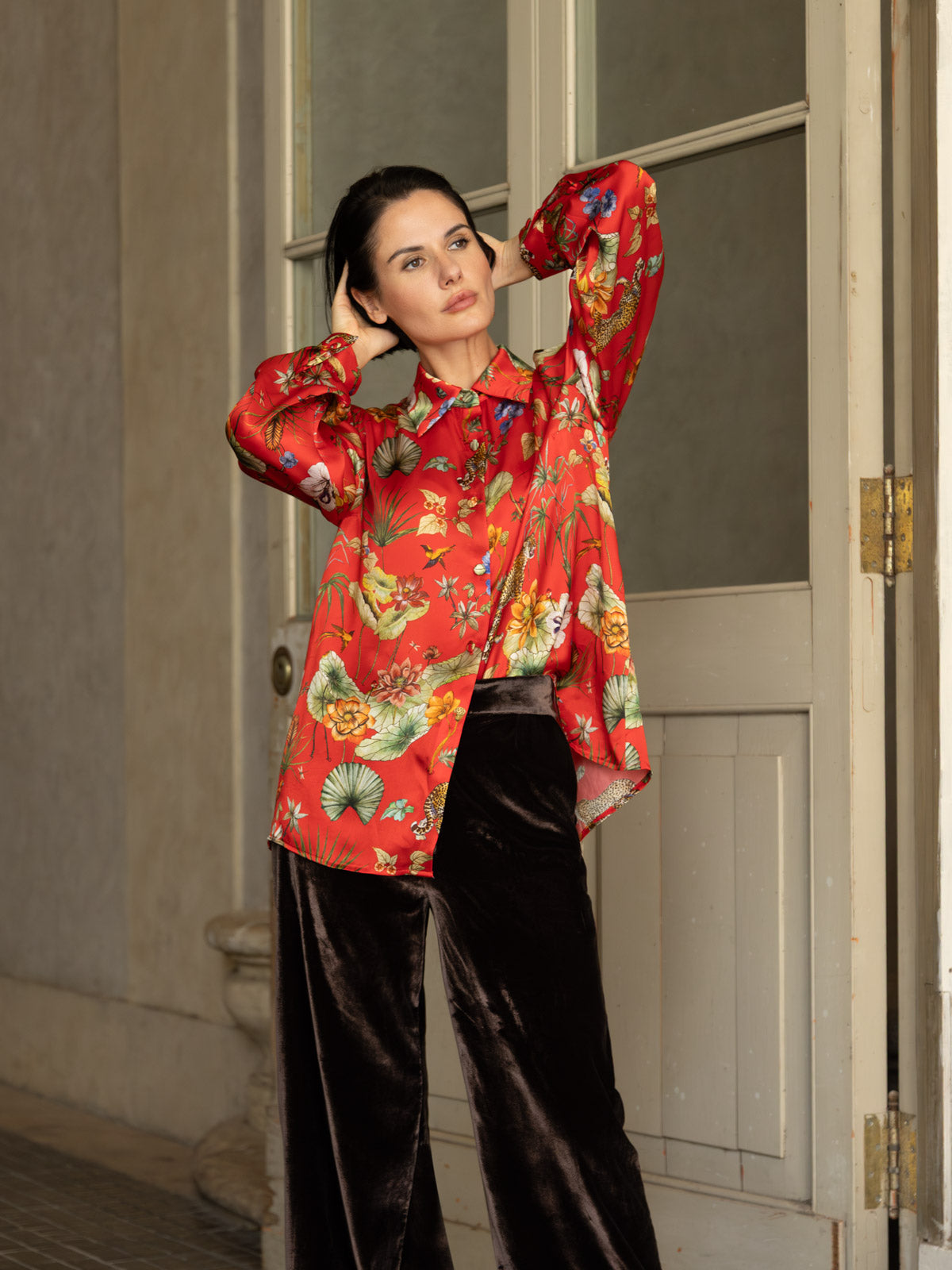 Camicia in seta rossa Horti Imperiali indossata da una donna, abbinata a pantaloni di velluto, in un ambiente elegante.