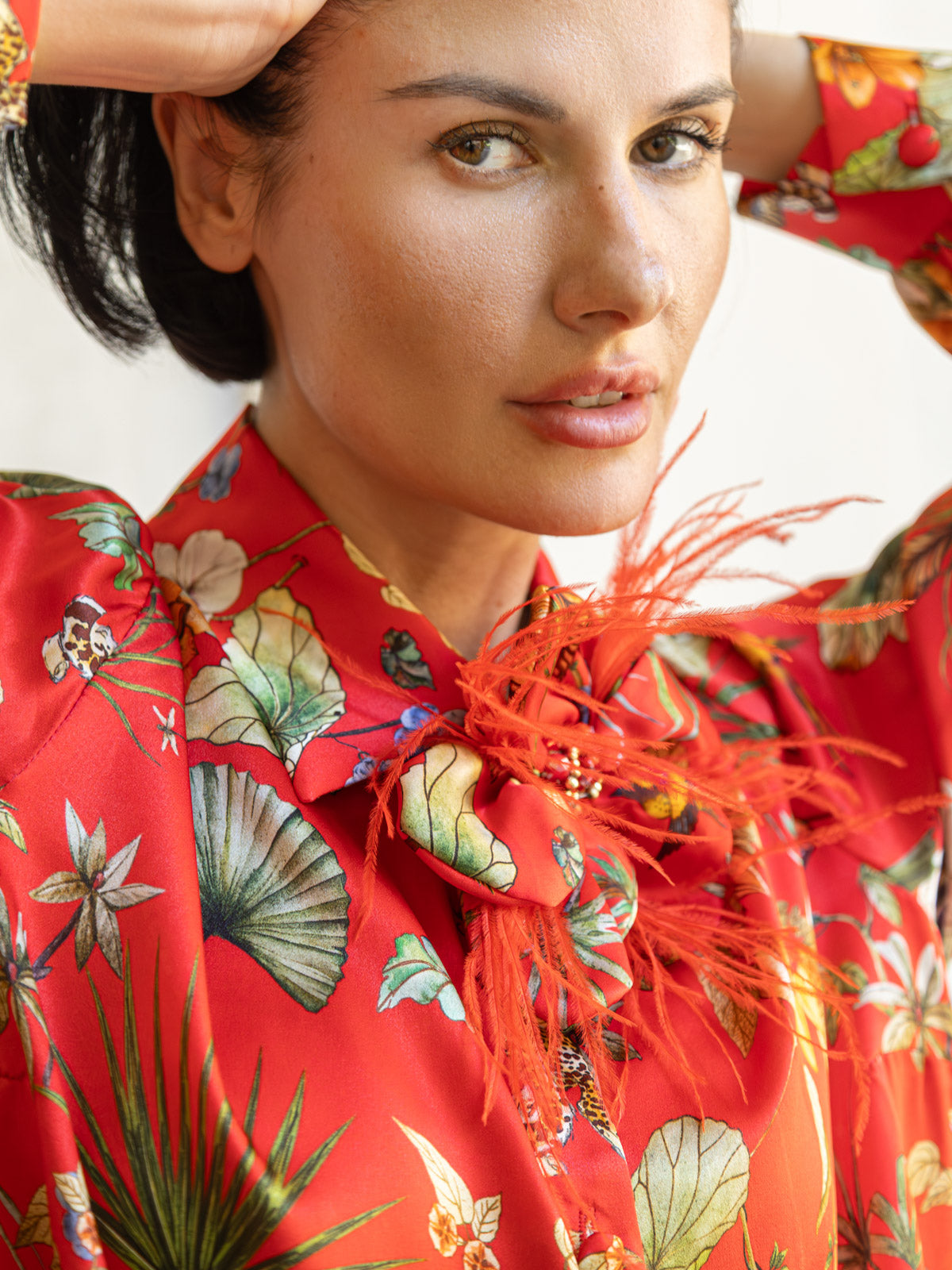 Dettaglio della camicia in seta rossa Horti Imperiali con stampa floreale e decorazioni in piume.