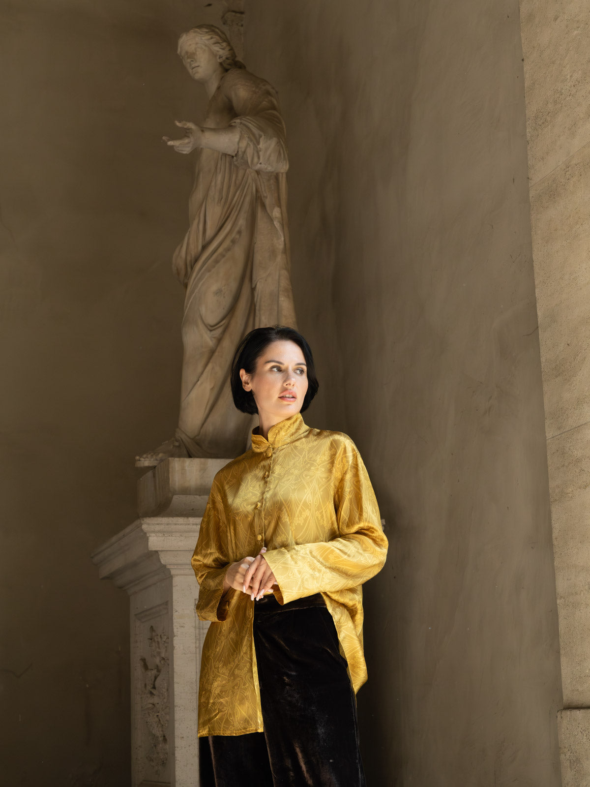 Camicia jacquard oro Domus Aurea indossata da una donna davanti a una statua.