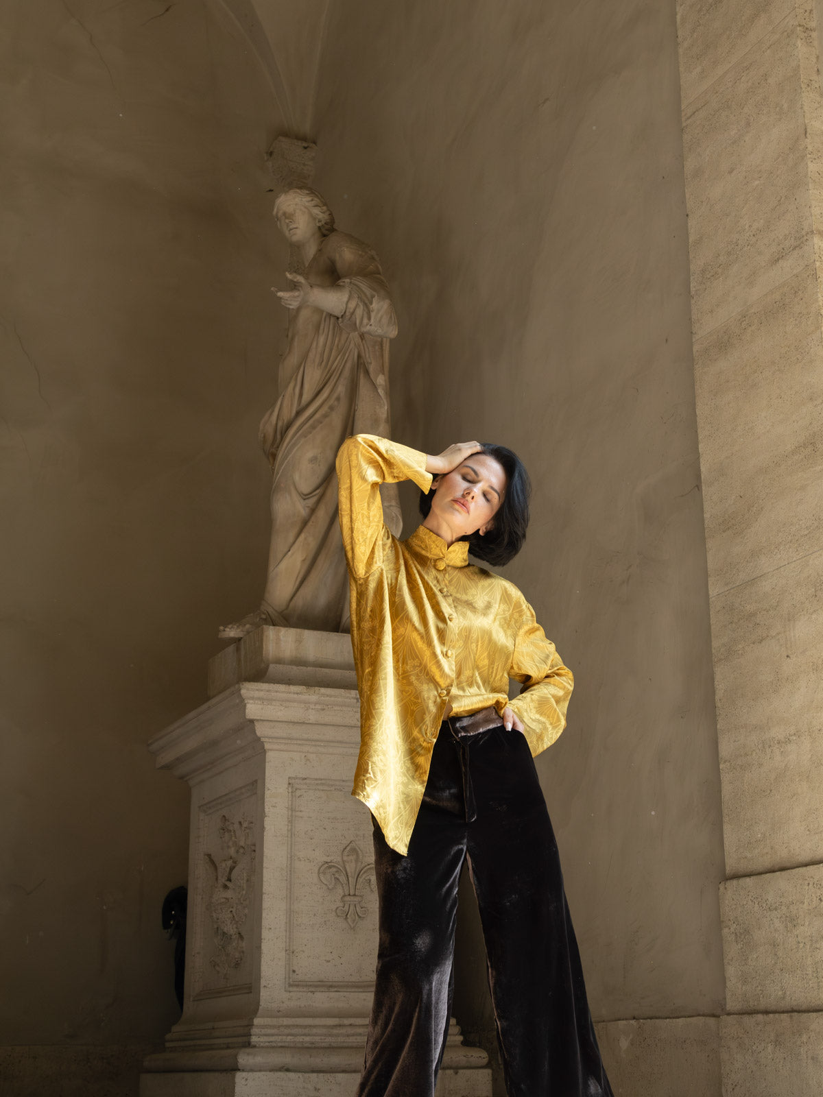 Modella che indossa la camicia jacquard oro Domus Aurea davanti a una statua in un ambiente elegante.