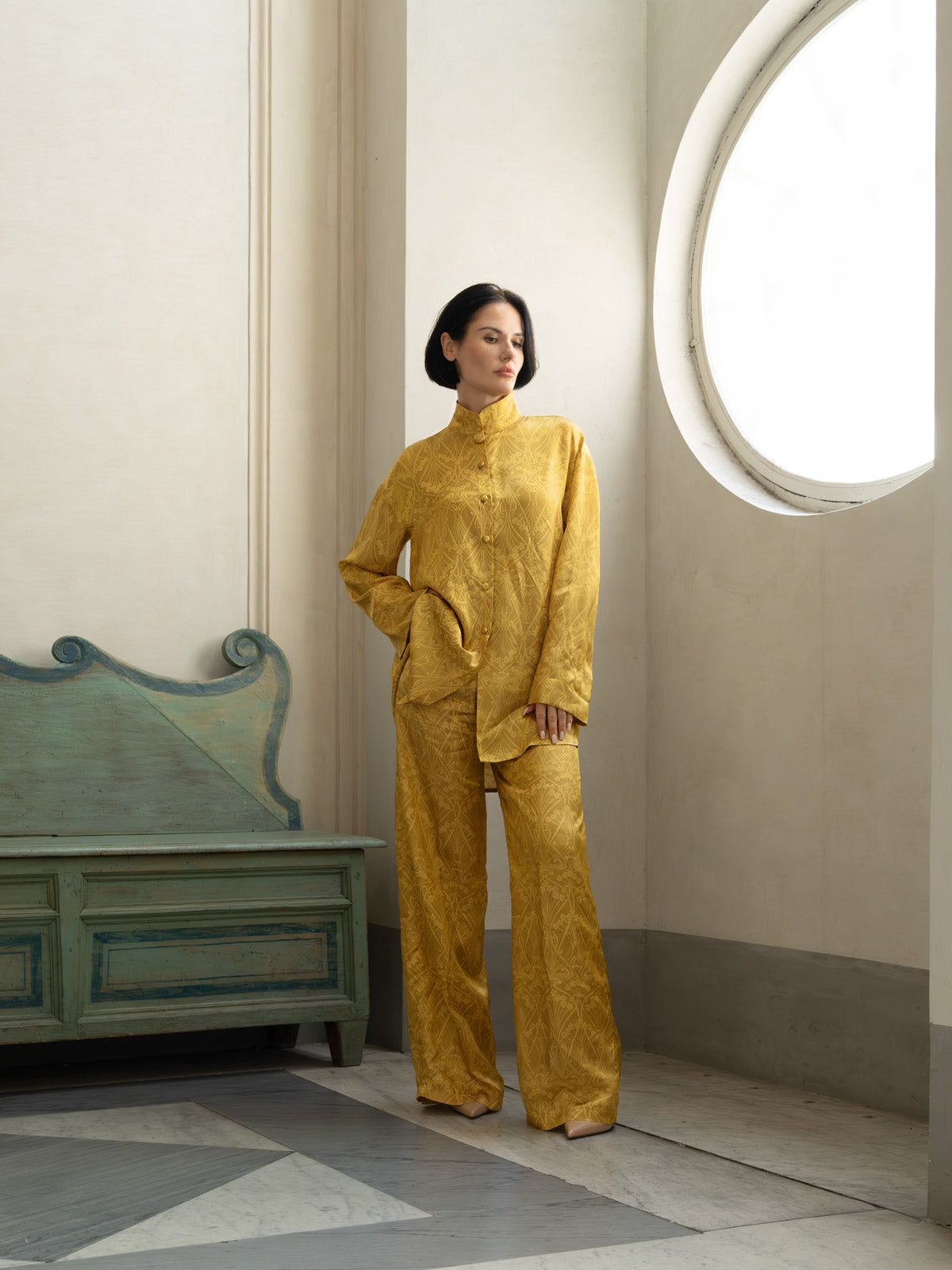 Modello indossa pantalone palazzo viscosa oro champagne in un ambiente elegante.