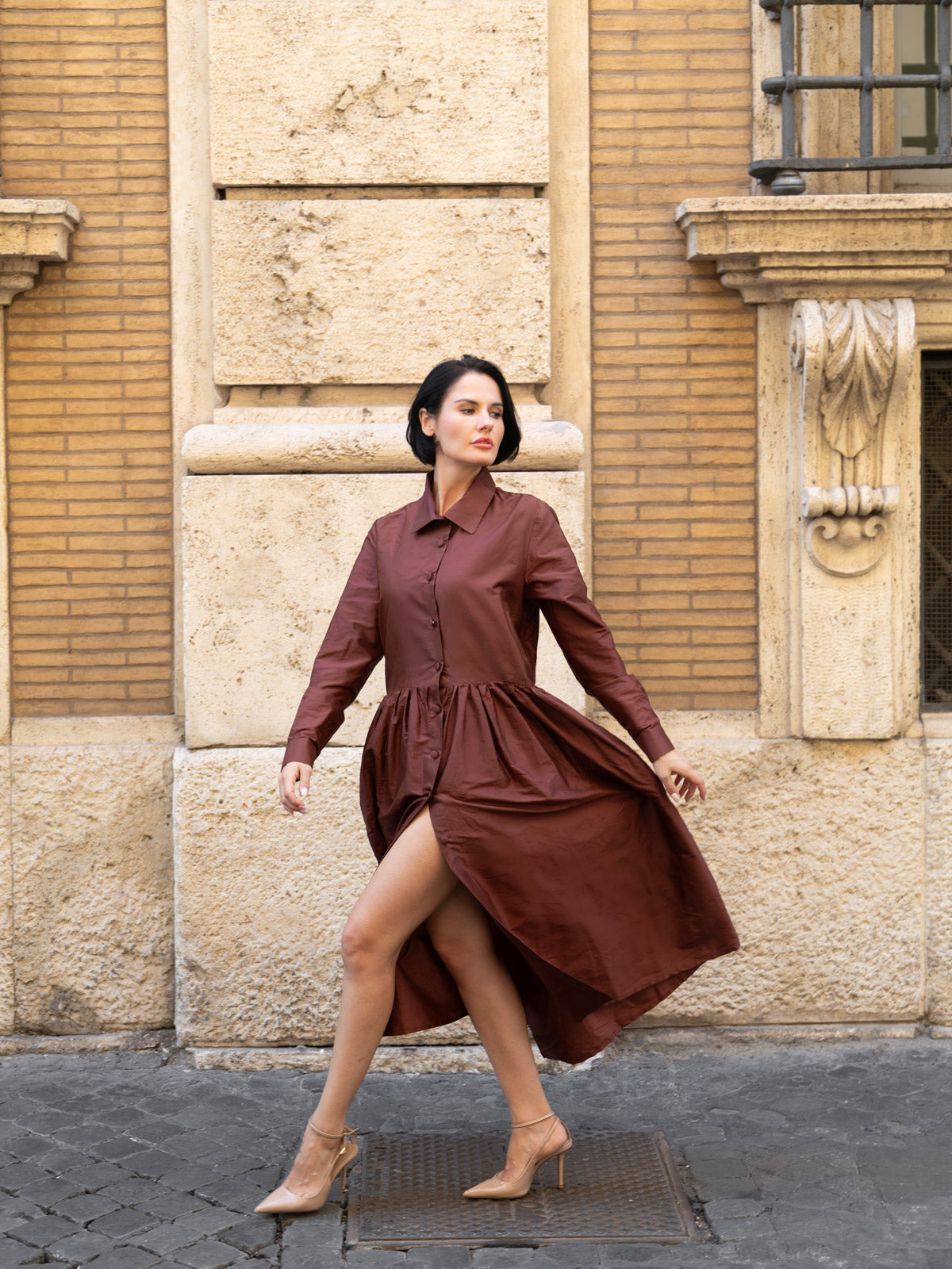 Abito in shantung elegante marrone indossato da una donna in una strada romana.