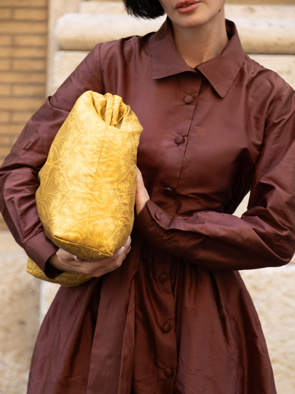 Sofia Marrone in abito in shantung elegante, con borsa gialla in mano, posa con eleganza.