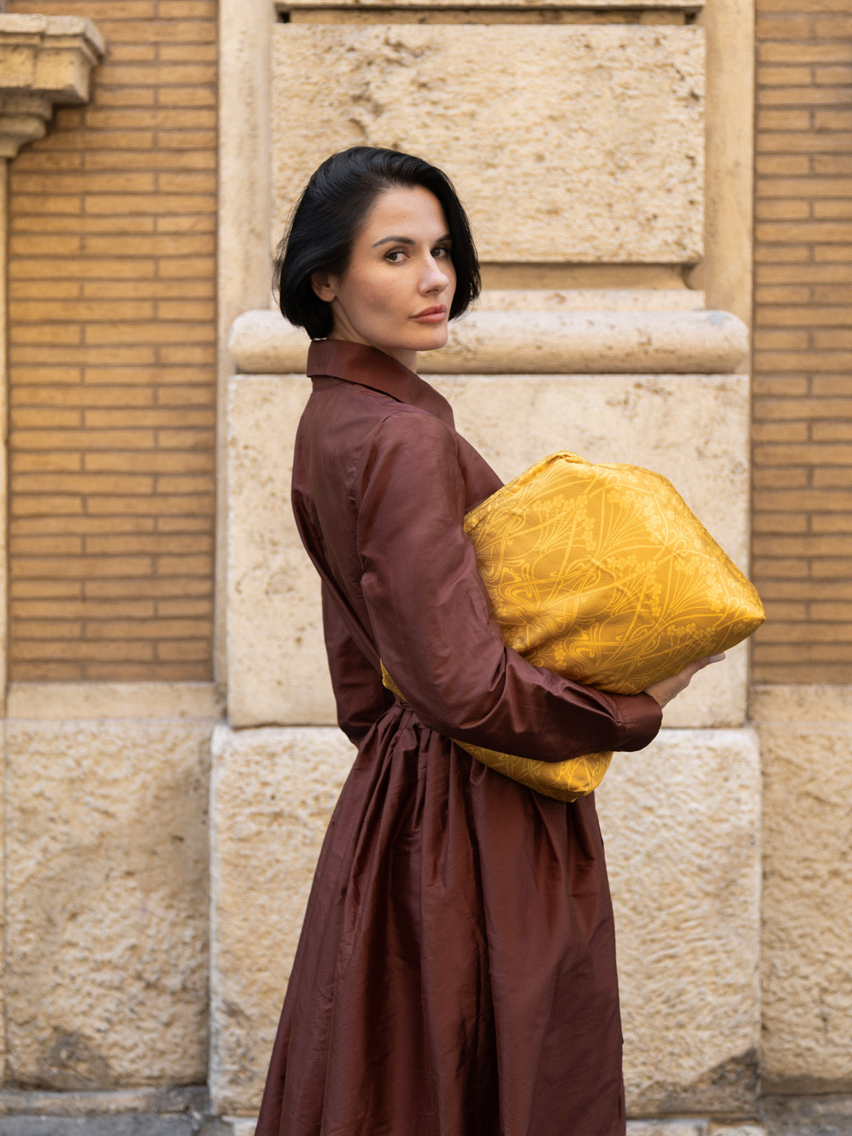 Moda: donna con maxi clutch floreale Liberty in tessuto dorato e abito marrone.