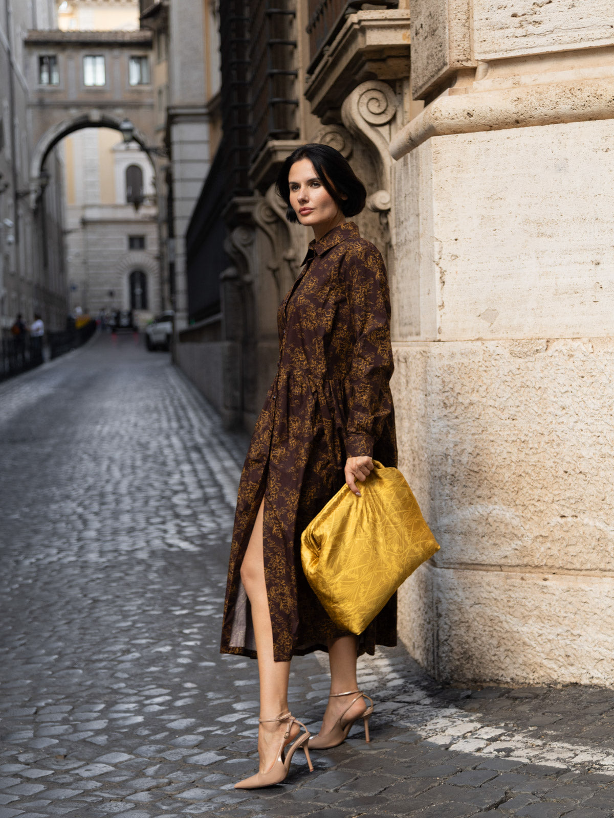Donna elegante con maxi clutch floreale Liberty in una strada storica, indossando scarpe con tacco.