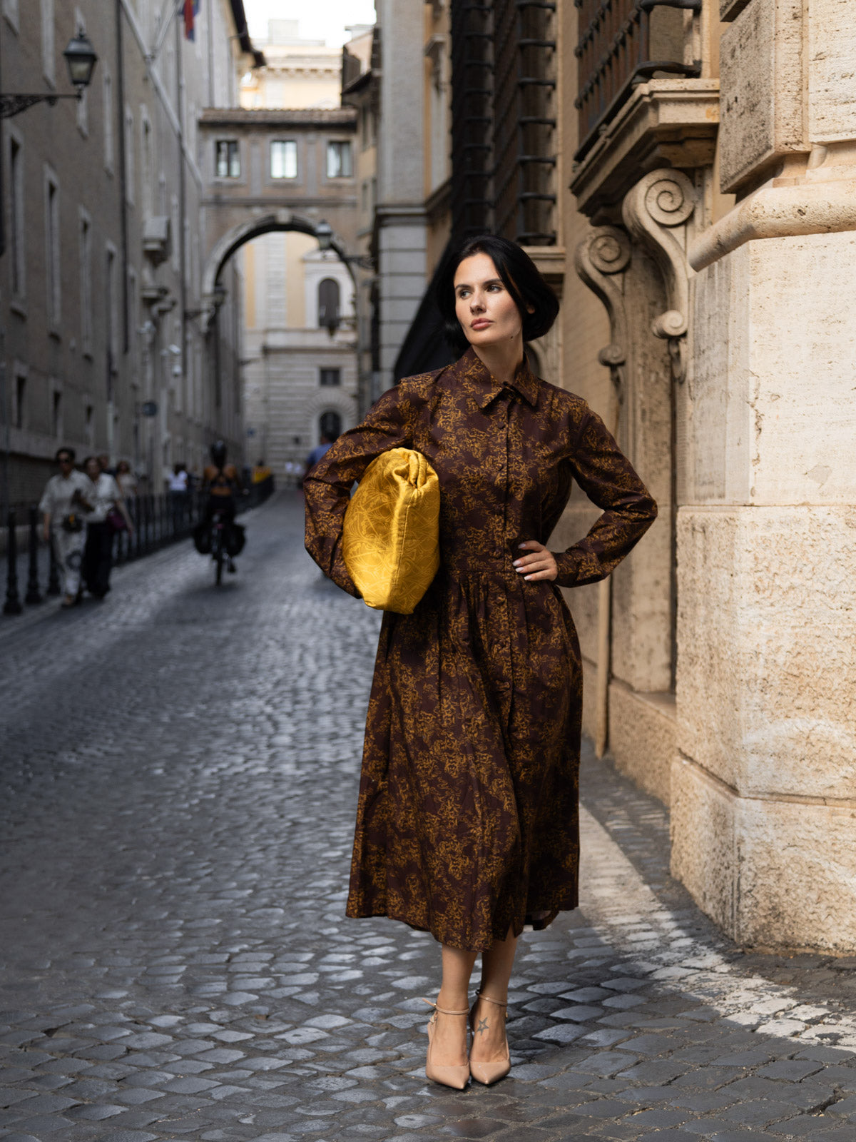 Modella in abito lungo con maxi clutch floreale Liberty mentre passeggia in una strada di Roma.