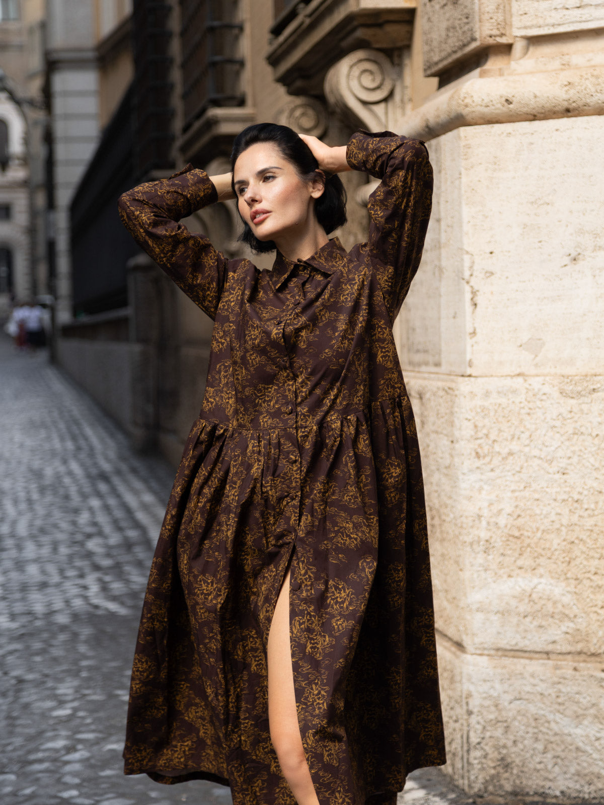 Modella che indossa un abito lungo in tessuto Liberty con maniche lunghe e stampa botanica, posando in una strada storica.
