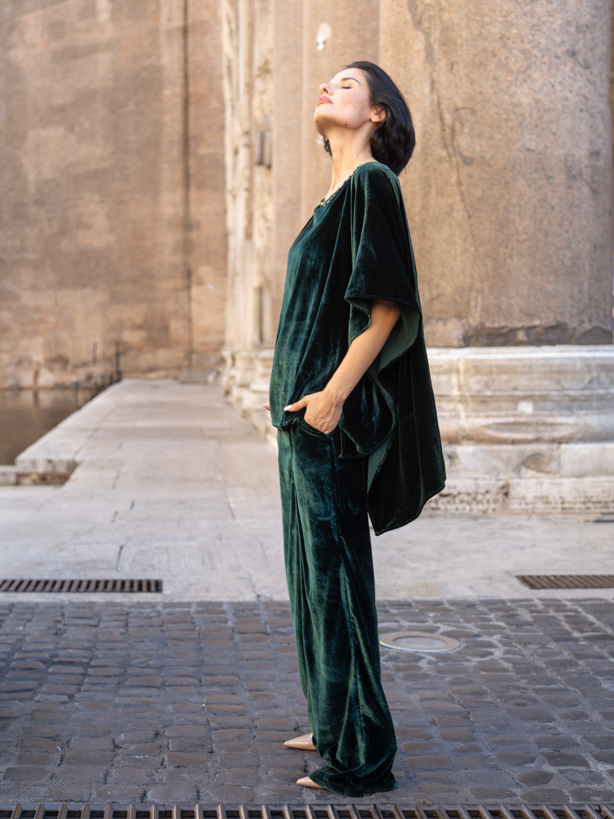 Modella in casacca velluto italiano verde bosco, abbinata a pantaloni coordinati, in ambiente urbano.