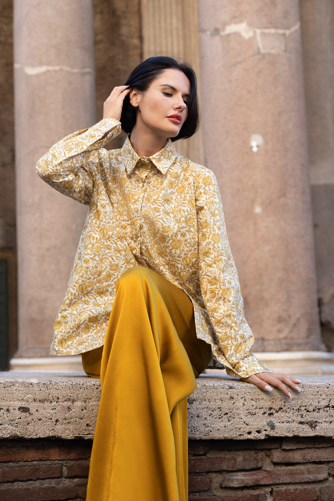 Camicia Liberty in cotone con elegante stampa floreale indossata da una donna in posa con gonna gialla.