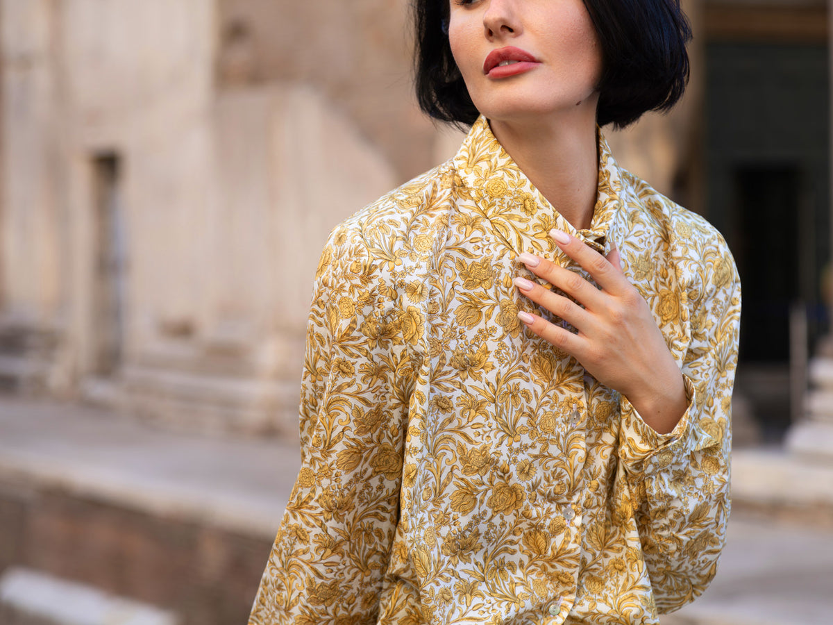 Donna che indossa una camicia Liberty in cotone con elegante stampa floreale in un ambiente storico.