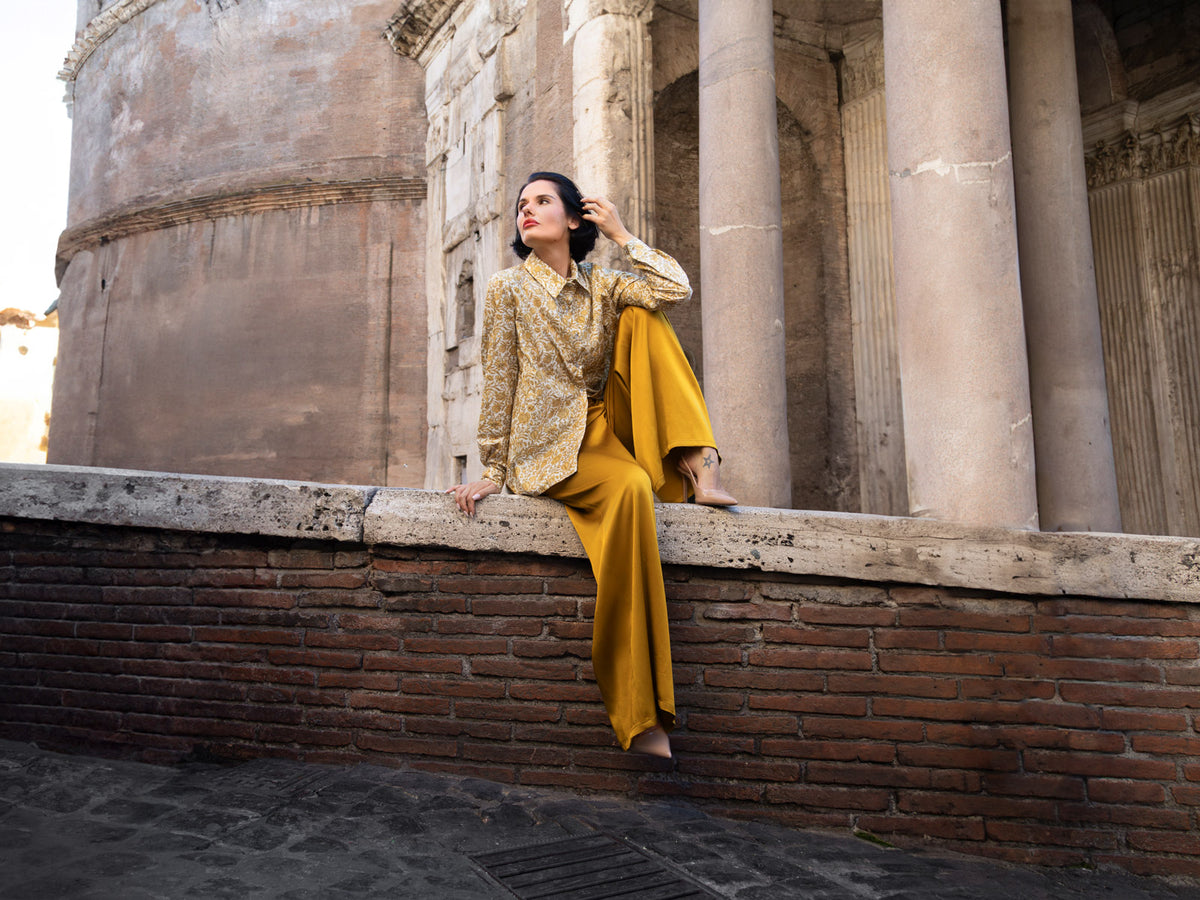 Donna elegante che indossa una camicia Liberty in cotone e pantaloni gialli in un ambiente architettonico raffinato.