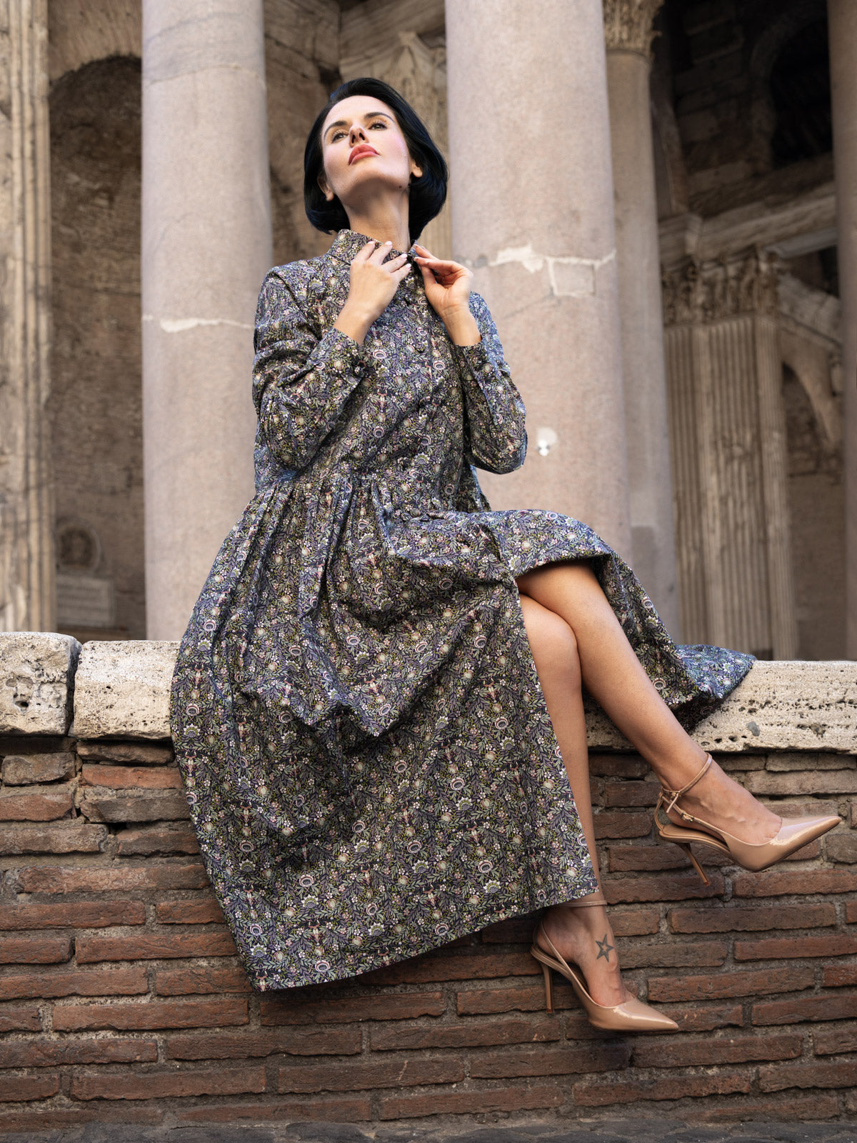 Modella che indossa abito lungo Liberty cotone, manica lunga e gonna a ruota, in un contesto architettonico elegante.