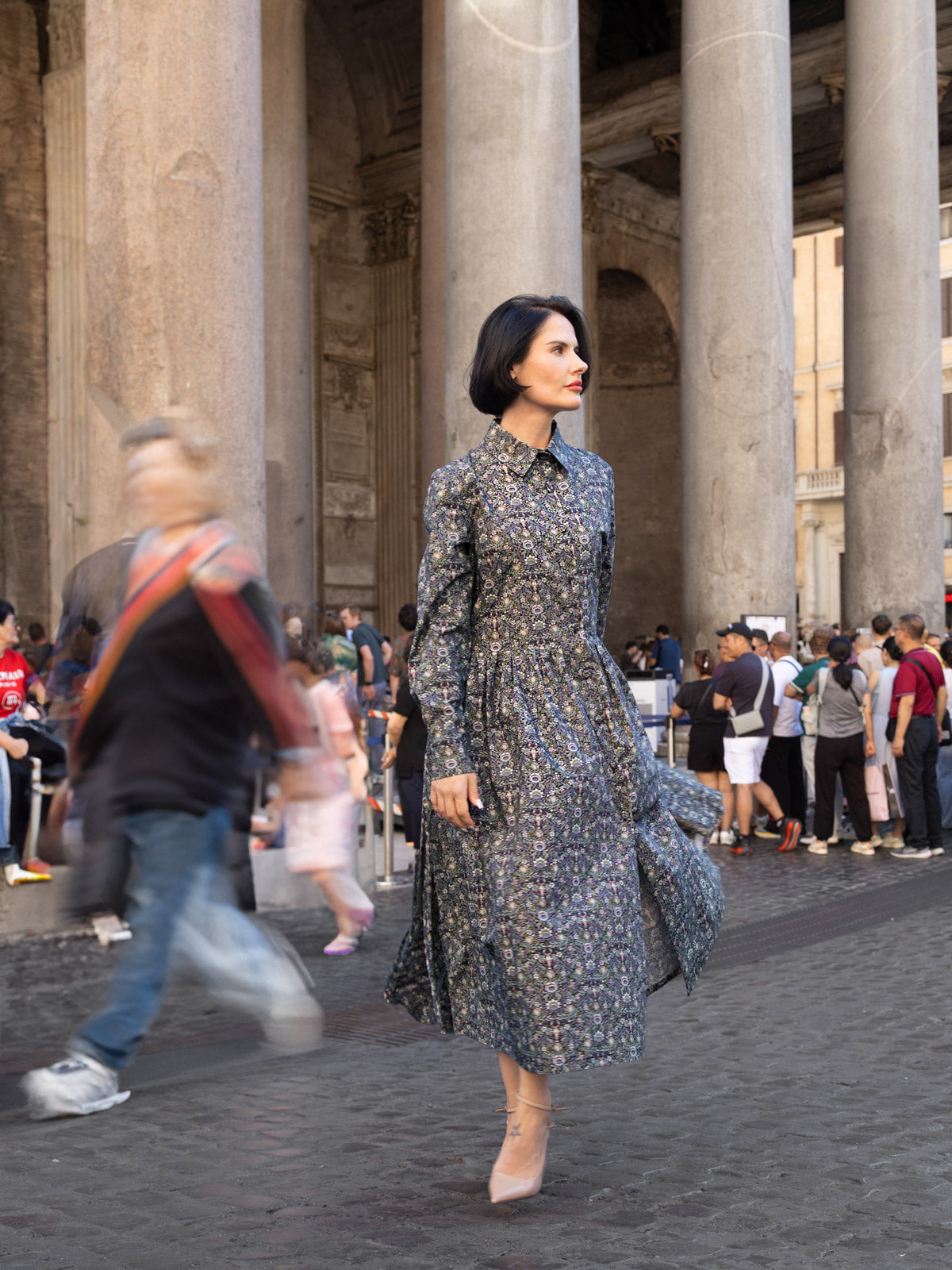 Abito lungo Liberty cotone indossato in una piazza affollata, evidenziando eleganza e stile.